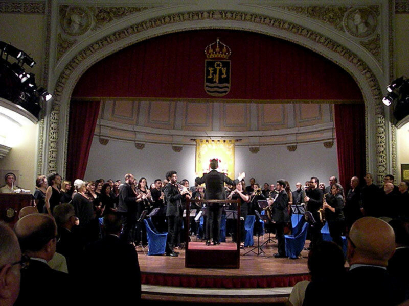 Orquesta de jazz en concierto en un teatro clásico con decoración elegante y audiencia atenta.