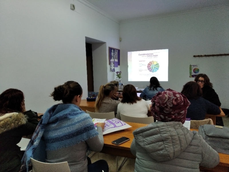 Alumnas en una clase, mirando un proyector con un diagrama de flujo. La sala tiene sillas y mesas, algunos estudiantes están tomando notas en cuadernos. La imagen sugiere un entorno educativo, posiblemente una conferencia o taller.