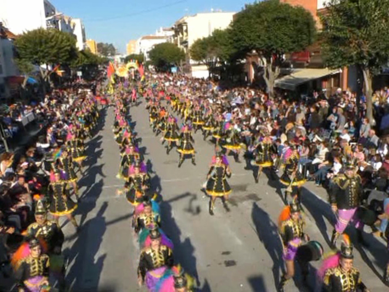 Desfile de carnaval en una calle con participantes vestidos con trajes tradicionales y multitud de espectadores.