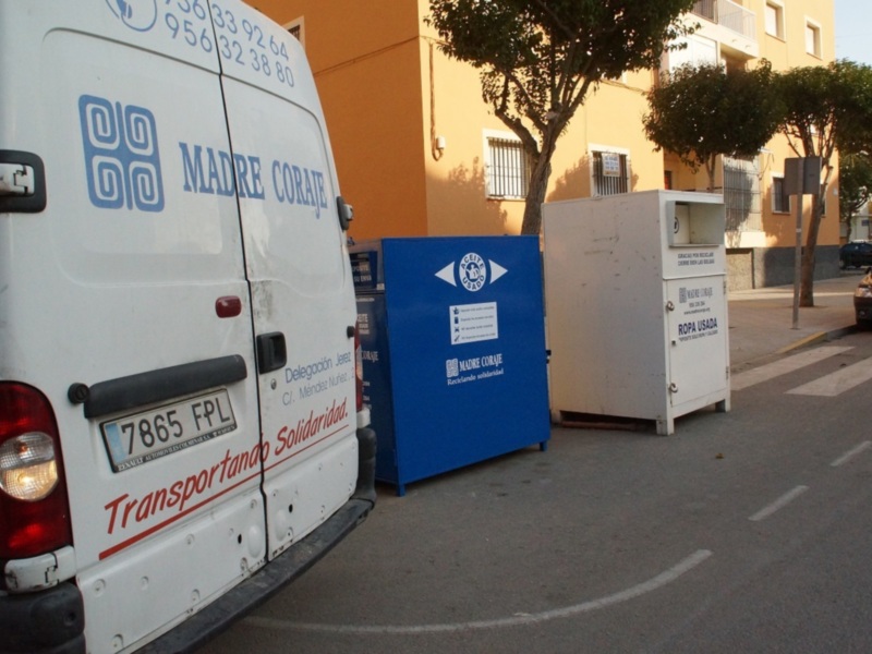 Vehículo de recolección de ropa usada y contenedores de reciclaje en una calle urbana.