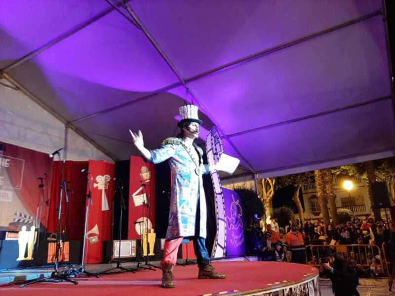 Actuación en escenario con decoración temática de cine, personaje vestido con traje de época y sombrero.