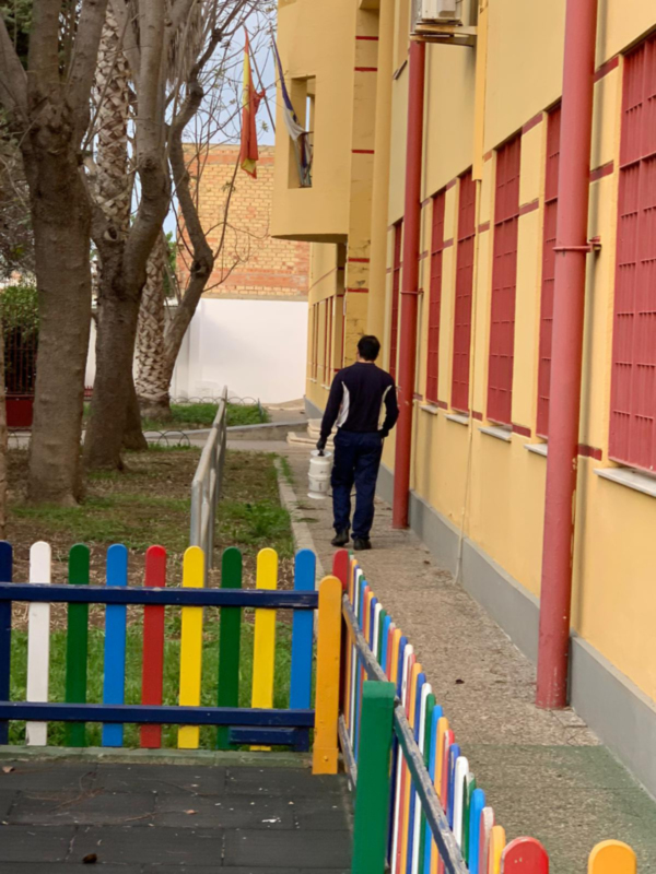 Persona caminando por un sendero junto a un edificio con banderas y una cerca de madera multicolor.