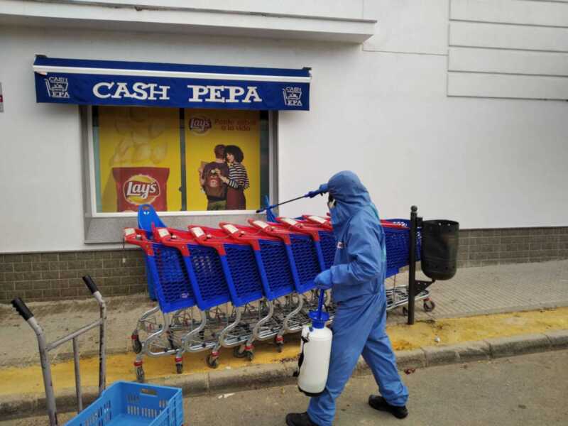 Personal en traje de protección desinfecta carros de compras en un supermercado Cash Pepa.