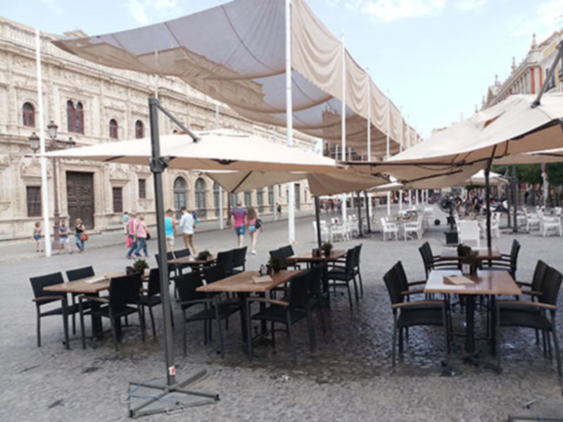 Un espacio abierto con mesas y sillas bajo grandes toldos, en una plaza con edificios históricos al fondo.
