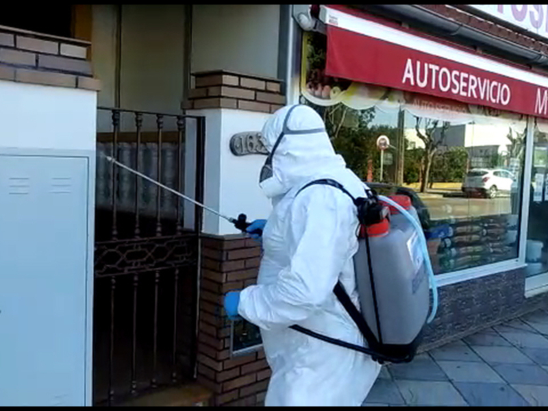 Un trabajador desinfecta una entrada de una tienda con equipo de protección personal.