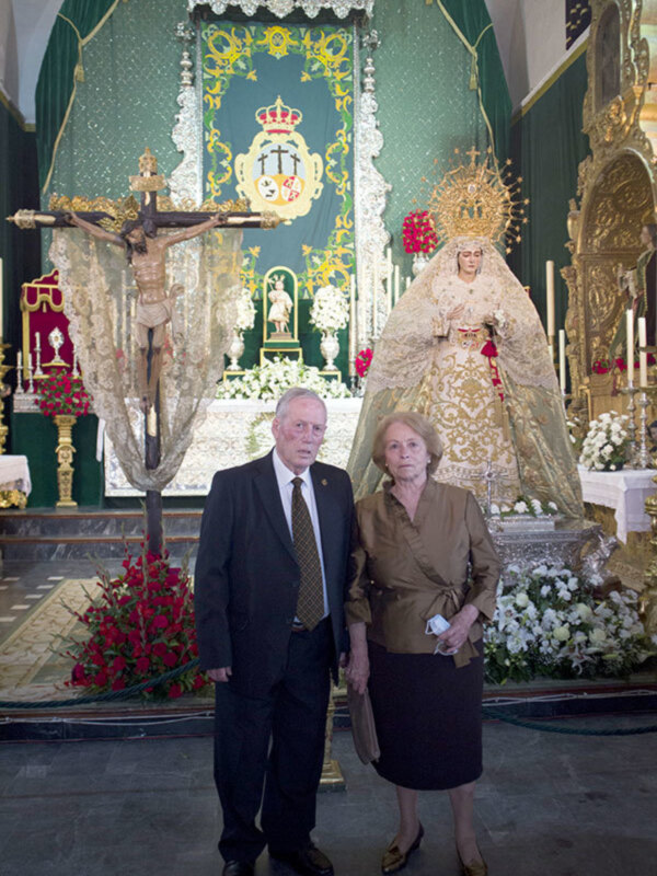 Retrato de pareja en un altar con la Virgen de la Cinta y el Cristo crucificado, en un entorno religioso.