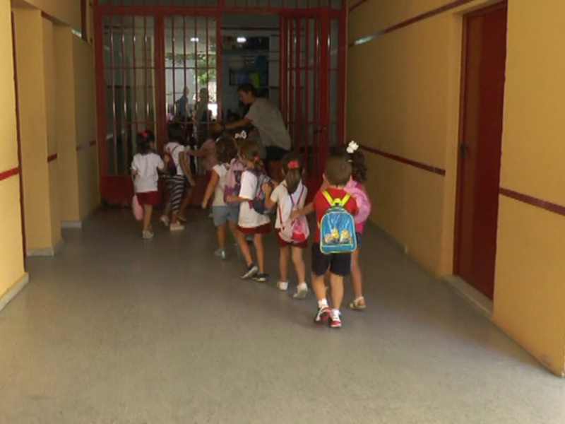 Niños caminando en un pasillo de escuela, con uniformes y mochilas.