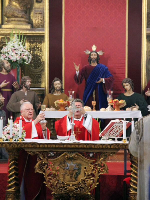 Elegante altar con estatuas religiosas y flores, iluminado por velas y un crucifijo en el centro.