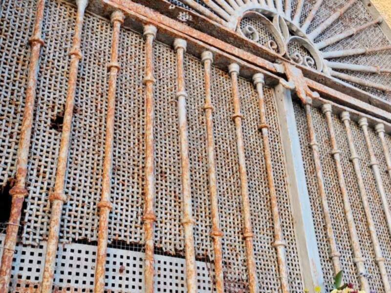 Puerta de hierro oxidada con detalles artísticos, frente a un edificio moderno.