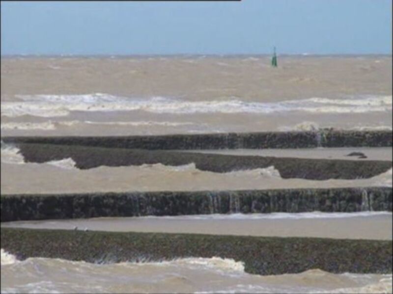 Una imagen de una playa con olas y un faro en el horizonte.