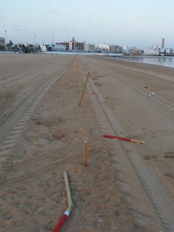 Una playa desierta con algunos palos de golf en el suelo, frente a una línea de edificios y un horizonte borroso.