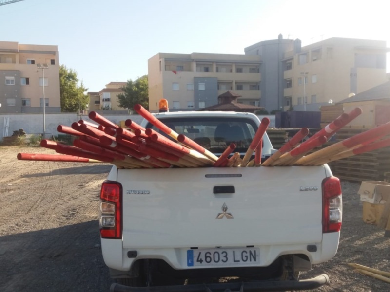 Un camión blanco con un remolque lleno de tubos rojos está estacionado en una zona residencial con edificios al fondo. La placa del vehículo es 4603 LGN.