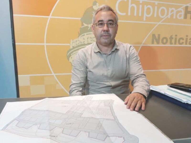 Un hombre sentado en una mesa con un mapa de una ciudad en el frente, frente a un fondo con el logotipo de ChipiononaHoyNoticias.