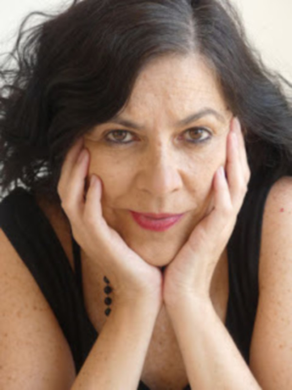 Retrato de mujer con cabello oscuro y manos apoyadas en la barbilla, con un fondo neutro.