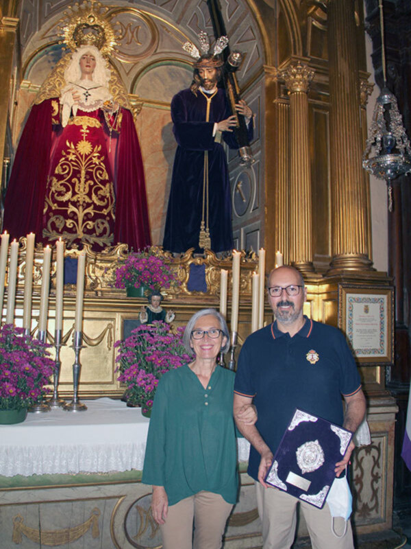Celebración religiosa en un templo con imágenes de santos y personas posando con un documento.