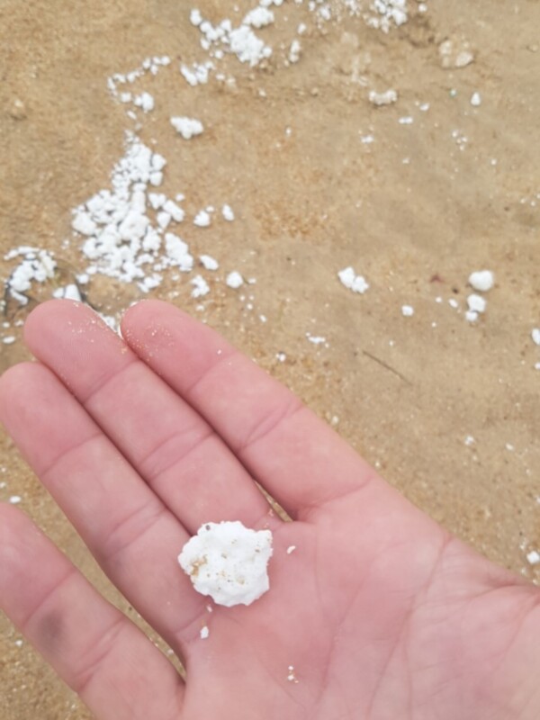 Una mano sosteniendo una pequeña bola blanca en la arena de una playa.