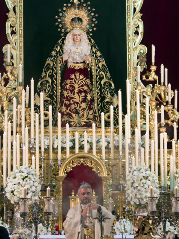 Procesión religiosa con la Virgen María en un altar ornado con candelabros y flores.