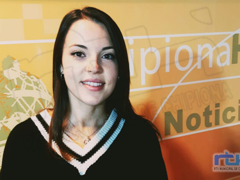 A una mujer con cabello largo y negro, sonriendo frente a un fondo amarillo con el texto "Noticias" en rojo. La mujer lleva una camiseta negra con detalles blancos y azules.