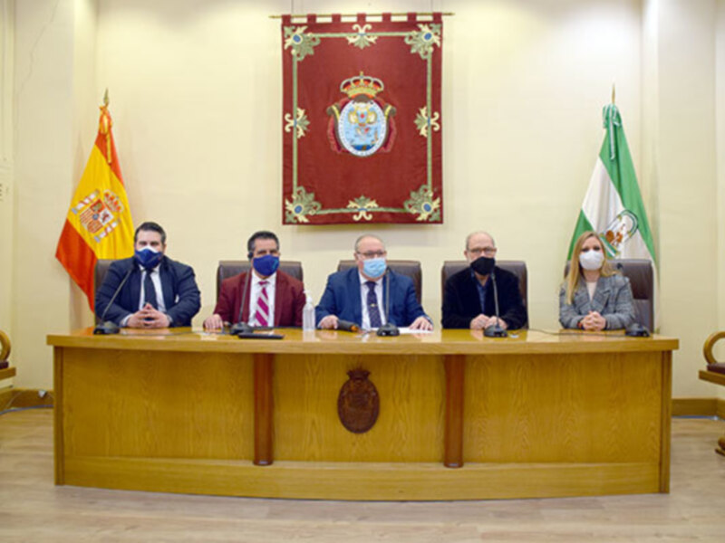 Reunión oficial con autoridades y representantes en un ambiente formal con banderas españolas y andaluzas.