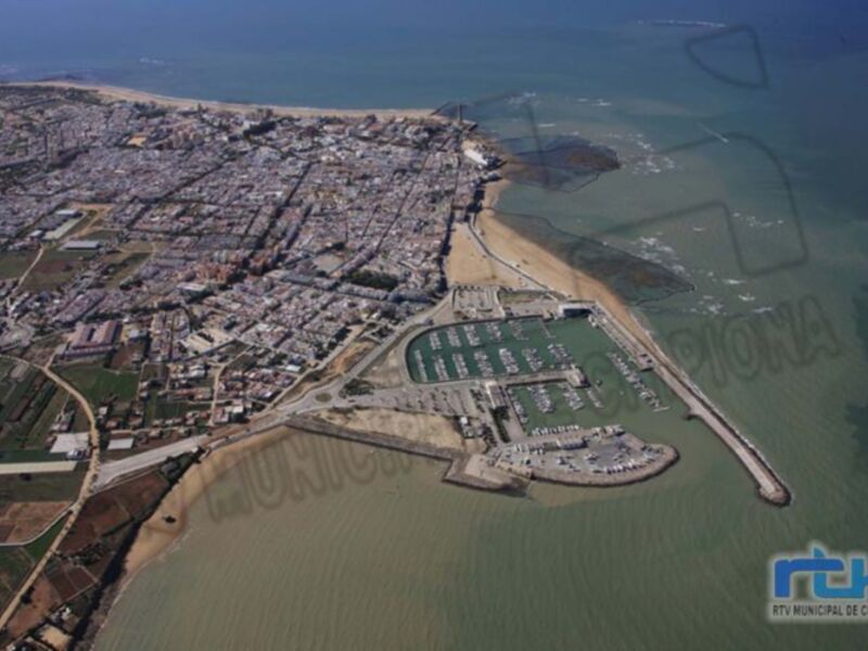 Imagen aérea de Chipiona, con una ciudad próxima al mar y un puerto.