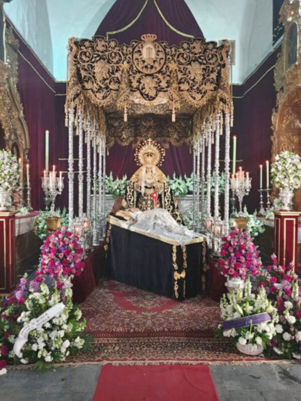 Altar con imagen de la Virgen María en una procesión religiosa, adornado con flores y candelabros.