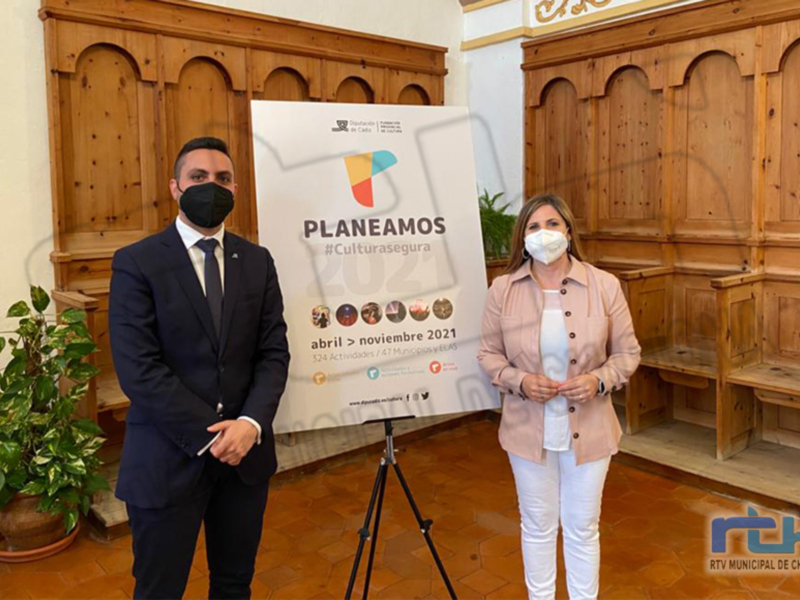 Dos personas en una sala con muebles de madera y un cartel informativo.