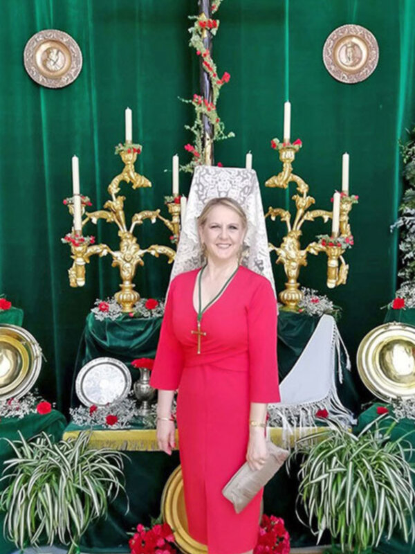 Una mujer sonríe frente a un altar adornado con cruces y candelabros dorados, rodeado de decoración festiva y platos de metal.