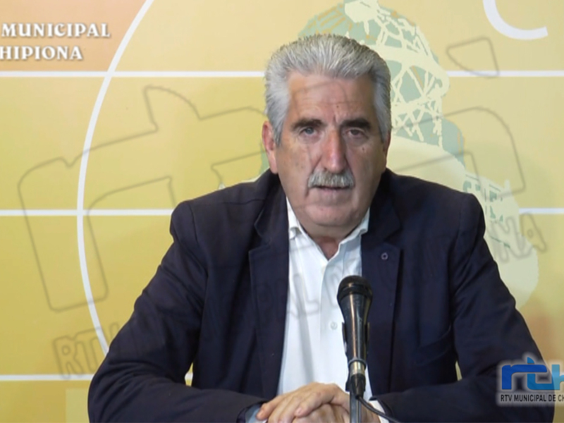 El pié de foto es un hombre sentado en una mesa con micrófonos, probablemente durante una conferencia o rueda de prensa. La imagen está en un fondo amarillo con una estructura geométrica y texturas de papel. En la parte superior izquierda, hay texto que dice "RTV MUNICIPAL CHIPIONA". En la parte inferior derecha, hay un logotipo de "RTV MUNICIPAL".