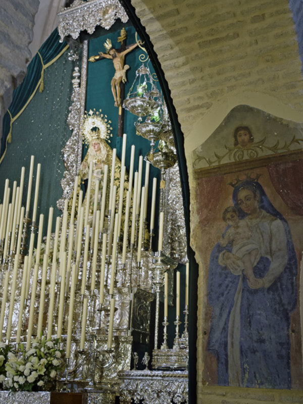Interior de una iglesia con una imagen de la Virgen María y el Niño Jesús, adornada con velas y decoración religiosa.