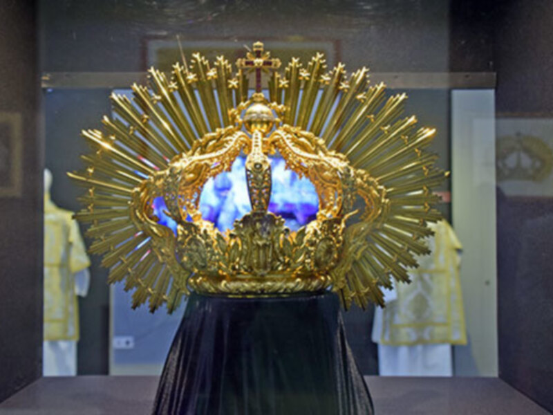Imagen de una corona dorada con rayos brillantes, posiblemente en un contexto religioso o ceremonial, con una figura central que parece ser una imagen de la Virgen María.