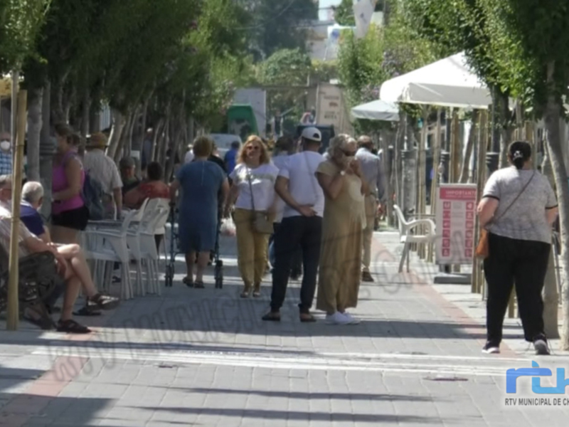 Calle con árboles y personas caminando y sentadas en mesas al aire libre.