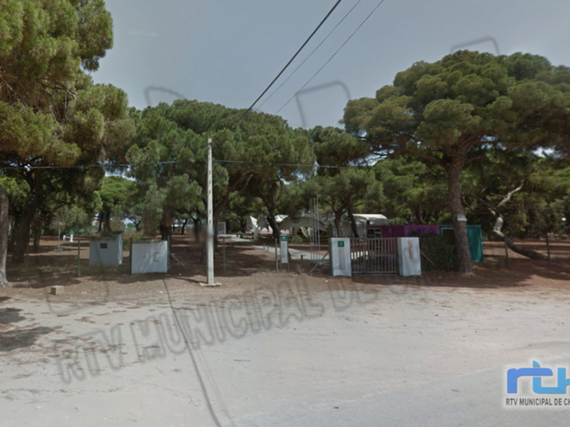 Área verde con pinos y valla de acceso, ubicación municipal en Chipiona.