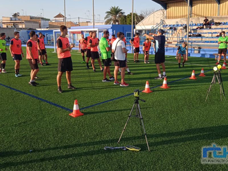 Entrenamiento de fútbol en un campo de césped artificial con jugadores y entrenador.
