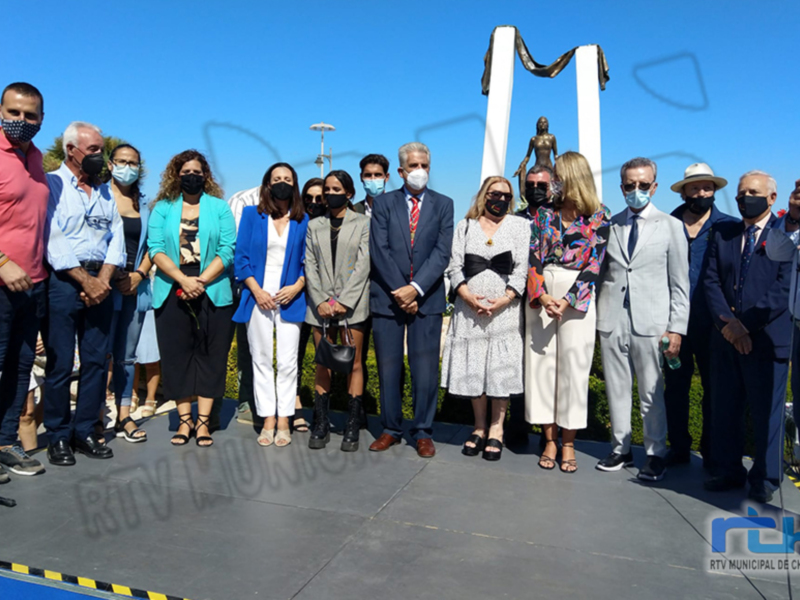 Una reunión formal de varios hombres y mujeres, todos vestidos con trajes o ropa formal. La imagen muestra a una persona en el centro, posiblemente la líder o anfitrión de la reunión. El fondo es una superficie plana con un cielo azul claro.
