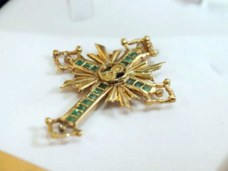 Joven broche dorado con detalles de esmeraldas y una figura central en relieve.