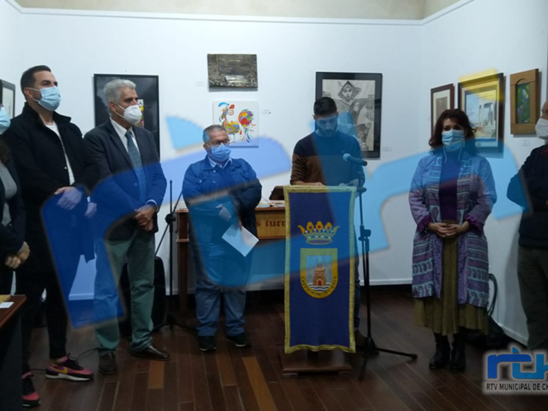 En una sala de conferencias, personas con máscaras médicas se encuentran en un ambiente formal. En el centro hay una figura con un gran escudo de armas y un documento sobre la mesa. La imagen transmite una reunión oficial o ceremonia de importantes eventos.