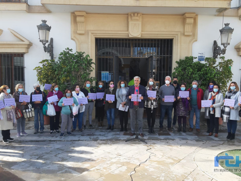 Gente con máscaras y pancartas frente a un edificio con un escudo en la puerta. La gente parece estar en una protesta o manifestación.