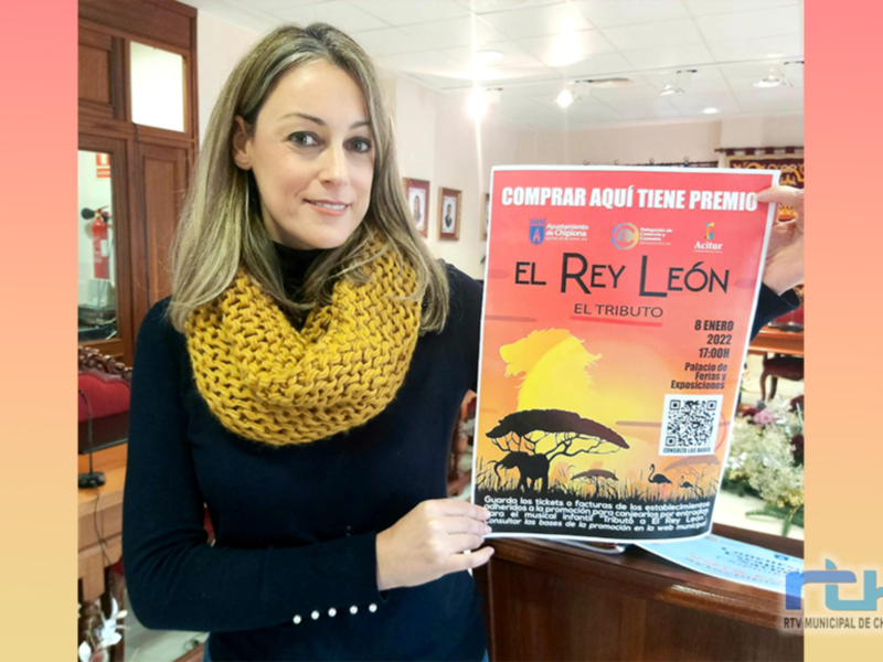 A una mujer sonriendo mientras sostiene un cartel promocional para "El Rey León: El Tributo". La fecha del evento es el 8 de enero de 2023, y se celebra en la Plaza de España de Chipiona. El cartel incluye detalles sobre el evento, como que se trata de un tributo y que es gratuito para los niños.