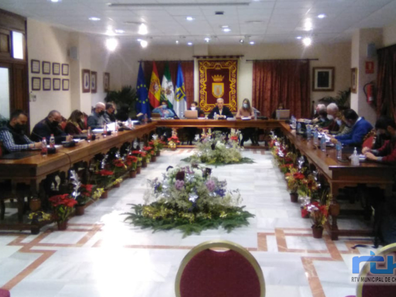 Sala de conferencias con mesas largas, sillas rojas, flores en el centro y banderas en la pared.