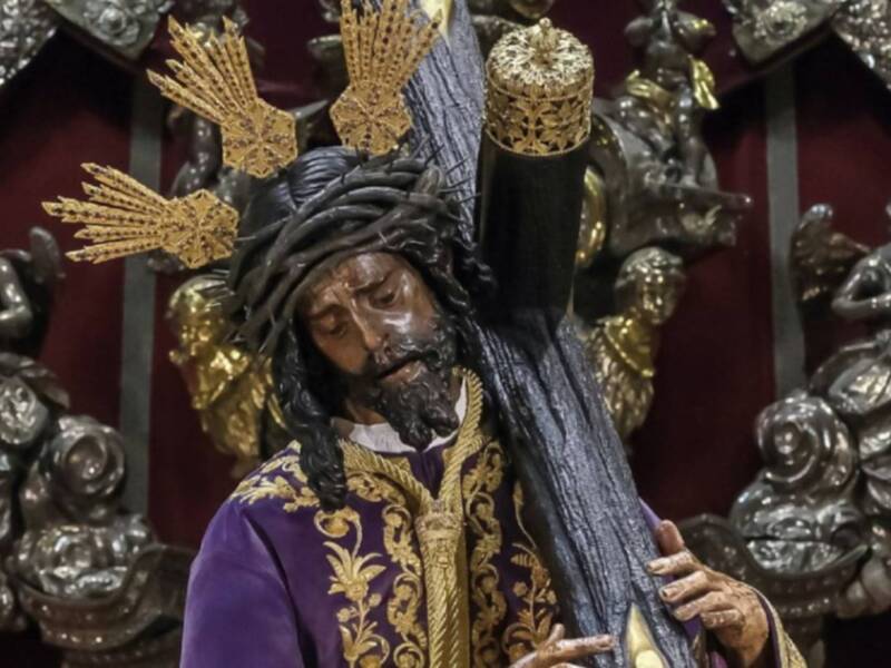 Imagen de un personaje religioso con vestimenta y tocado dorados, posiblemente una figura de Jesús. El fondo es oscuro con detalles metálicos.