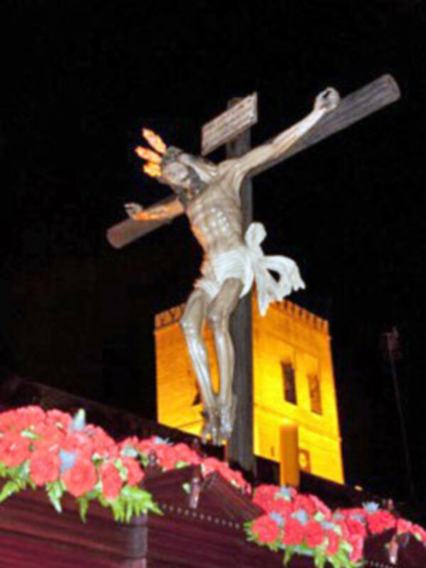 Representación de la crucifixión de Jesús en una procesión religiosa nocturna, adornada con flores rojas.
