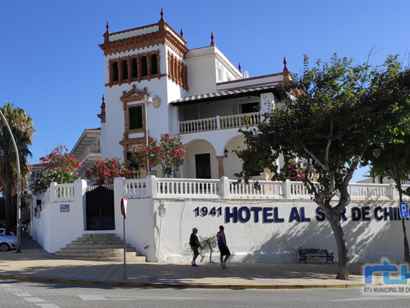 Hotel Al Sur de Chipiona, un edificio blanco con detalles rojos y flores rosadas, ubicado en Chipiona, España.