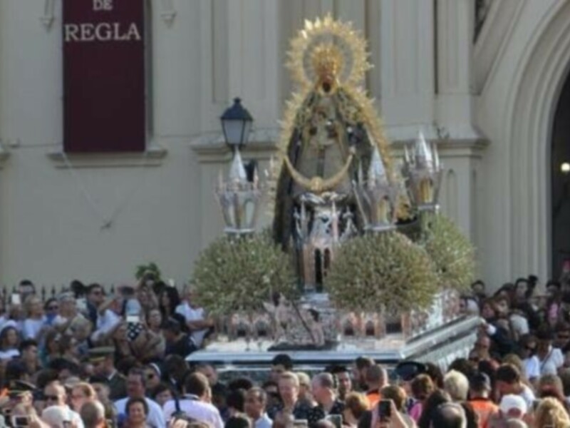 Procesión religiosa con imagen de la Virgen ante una multitud en una plaza histórica.