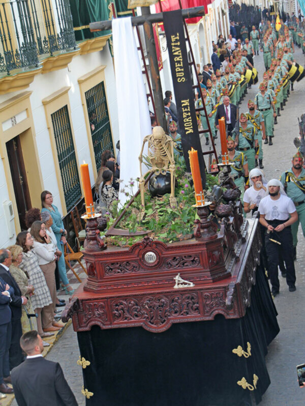 Procesión con paso de misterio en la Semana Santa de España, con una figura de un esqueleto y velas en un entorno urbano.