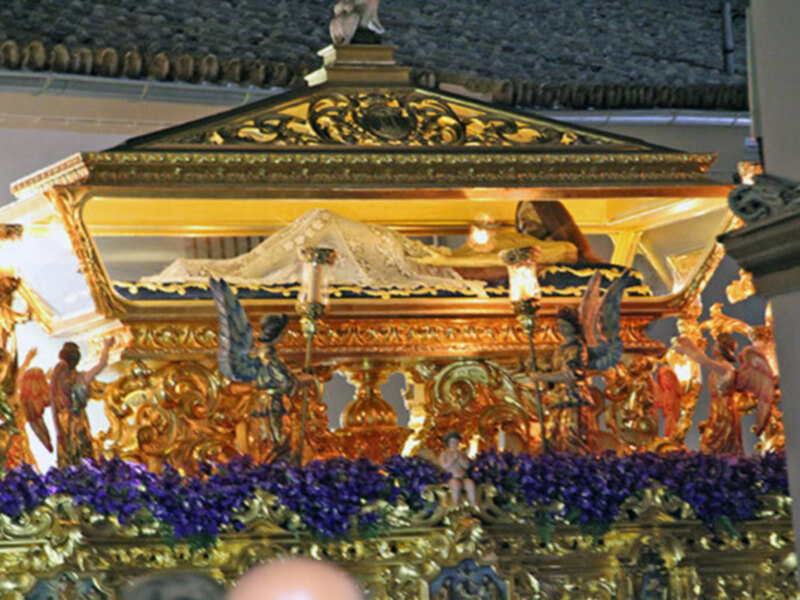 Un ataúd dorado y decorado con figuras religiosas, adornos dorados y flores azules.