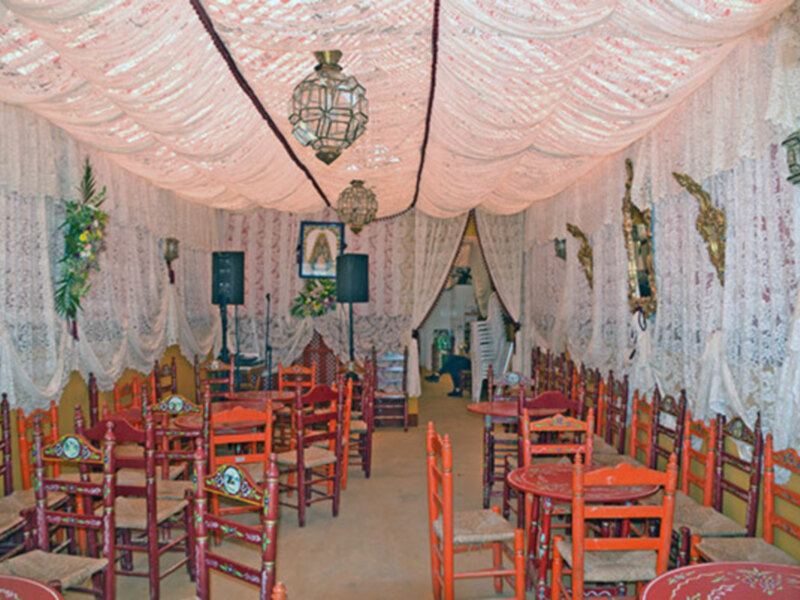 Una sala de comedor con sillas rojas y mesas redondas, decorada con cortinas blancas y adornos navideños. La iluminación es suave, creando un ambiente acogedor y festivo.