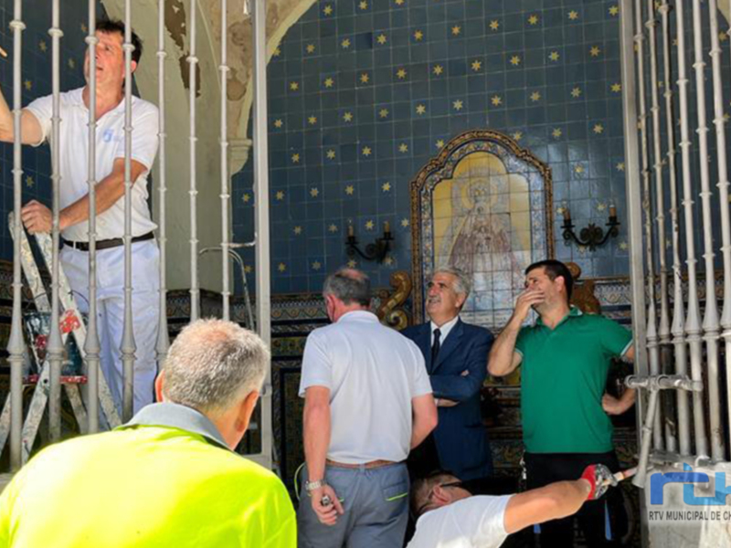 Un grupo de personas se encuentra frente a una imagen religiosa en un entorno decorado con azulejos y molduras. La escena parece ser una visita o un evento religioso en un edificio histórico.