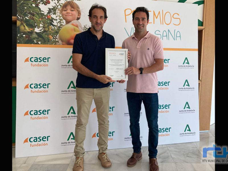 Dos hombres sostienen un premio junto a una pancarta con el logo de Caser y la frase "Premios Vida Sana".