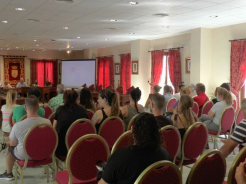 Una sala de conferencias con una pantalla proyectora y varias personas sentadas en sillas rojas.