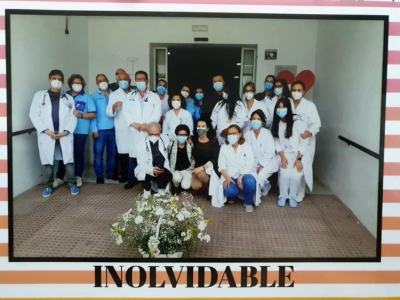 Grupo de médicos y enfermeras posando en un hospital. La imagen muestra a varios profesionales de la salud con máscaras faciales, posando frente a una puerta. En el fondo hay un balcón con plantas y un cartel que dice "INOLVIDABLE". La fotografía parece celebrar una importante fecha o aniversario.